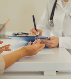 Médico con estetoscopio escribe en una tabla portapapeles durante una consulta